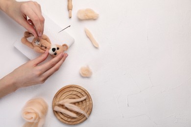 Photo of Woman felting toy bear from wool at white table, top view. Space for text