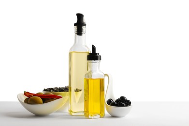 Bottles of different cooking oils, olives and sunflower seeds on white background