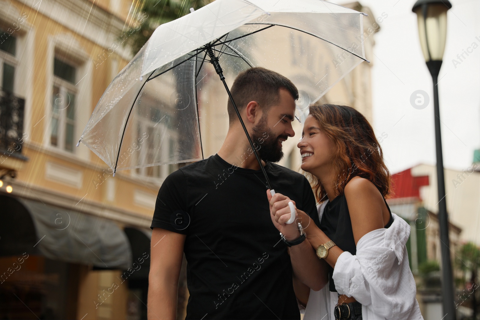 Photo of Young couple with umbrella enjoying time together under rain on city street