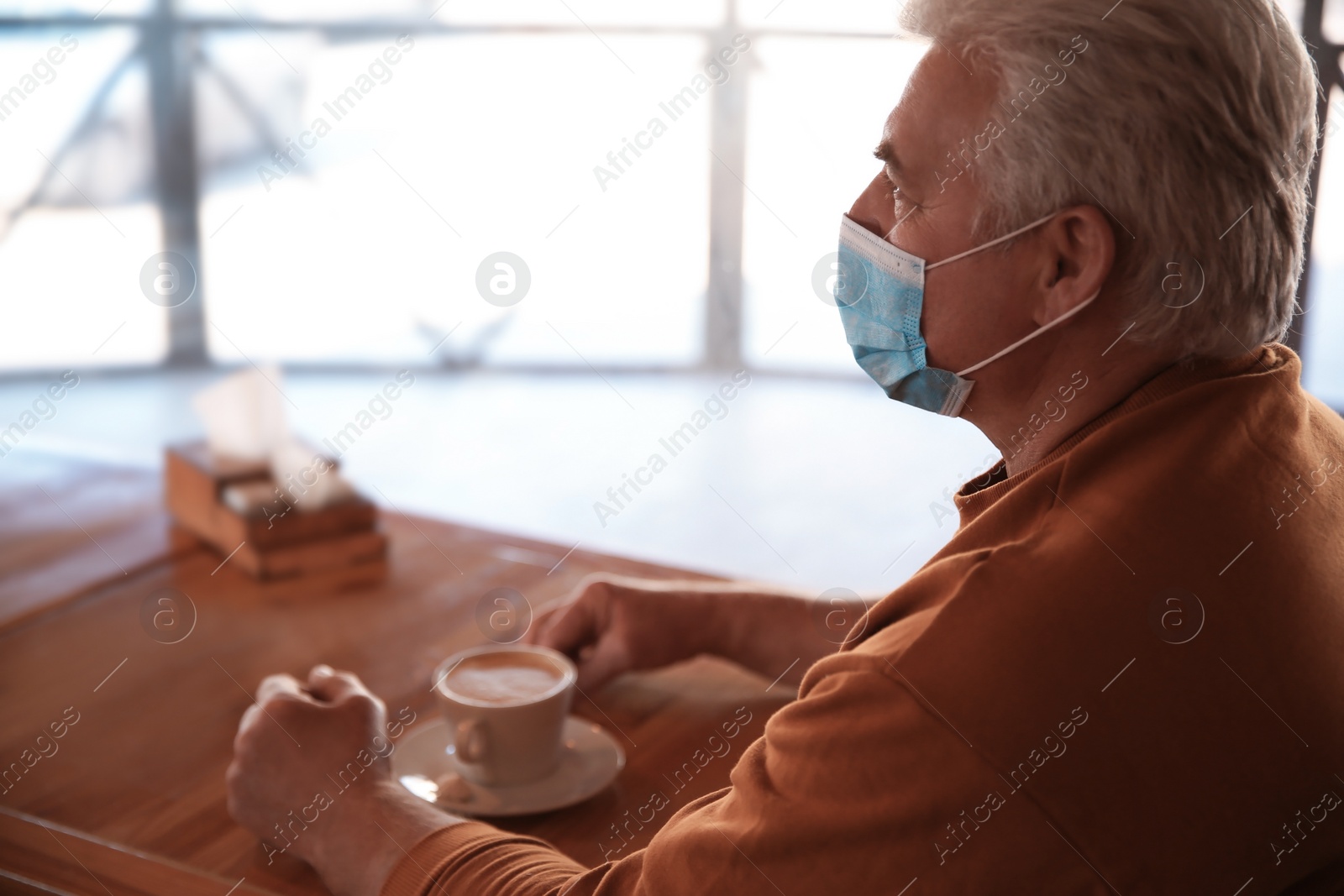 Photo of Senior man with medical mask in cafe. Virus protection