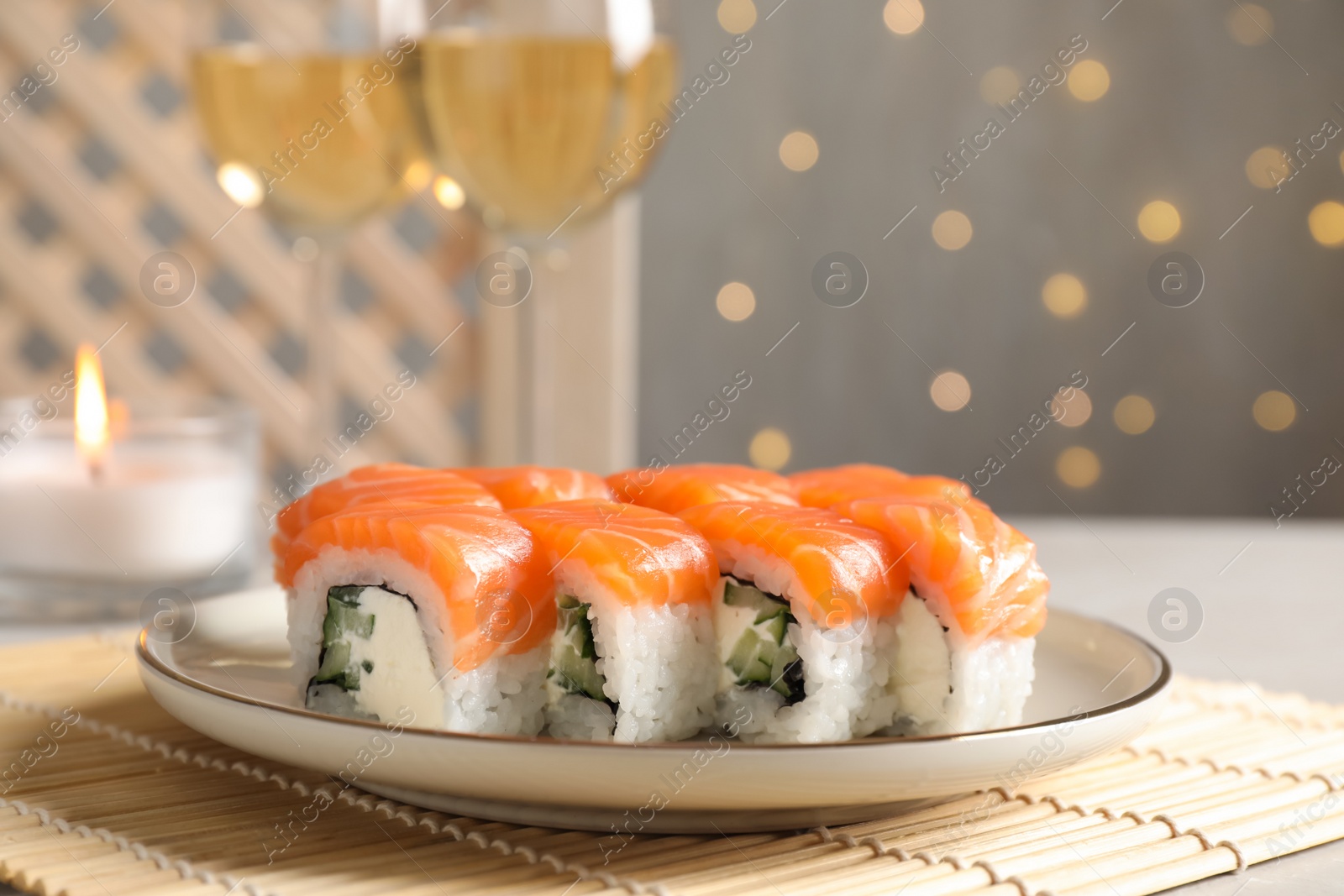 Photo of Tasty sushi rolls and glasses of wine on table against blurred lights, closeup
