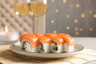 Tasty sushi rolls and glasses of wine on table against blurred lights, closeup