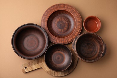 Photo of Ceramic bowls, wooden board and plate on beige background, flat lay