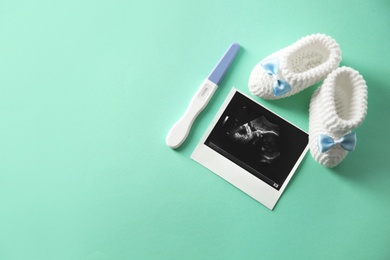 Ultrasound picture, baby shoes and pregnancy test on color background, top view with space for text