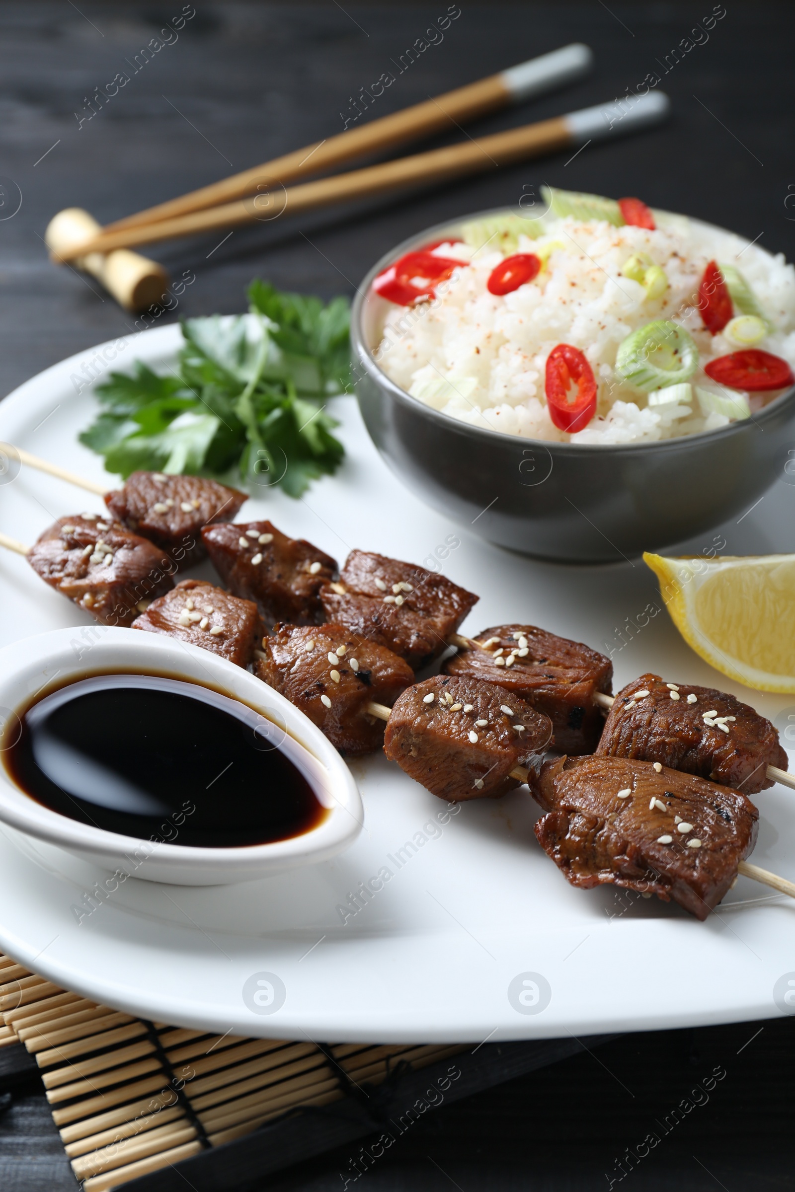 Photo of Tasty chicken meat glazed in soy sauce served with rice on black table, closeup