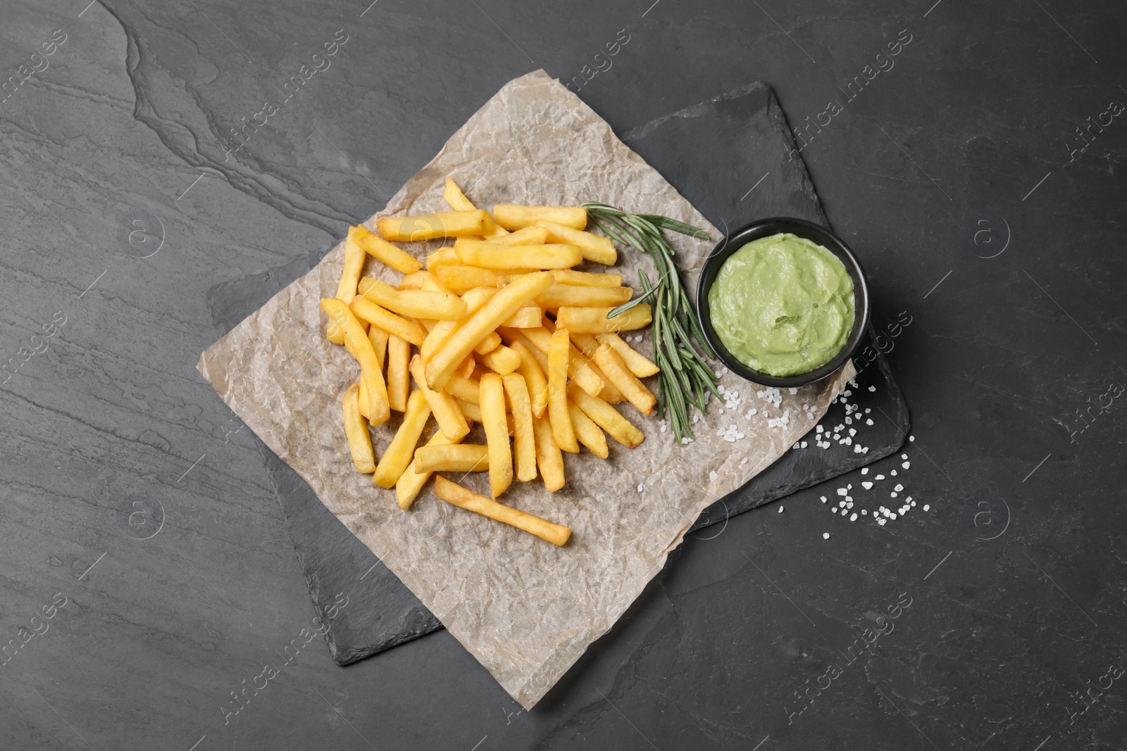 Photo of Serving board with french fries, guacamole dip and rosemary on black table, top view