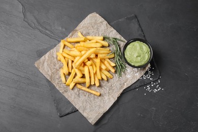 Photo of Serving board with french fries, guacamole dip and rosemary on black table, top view