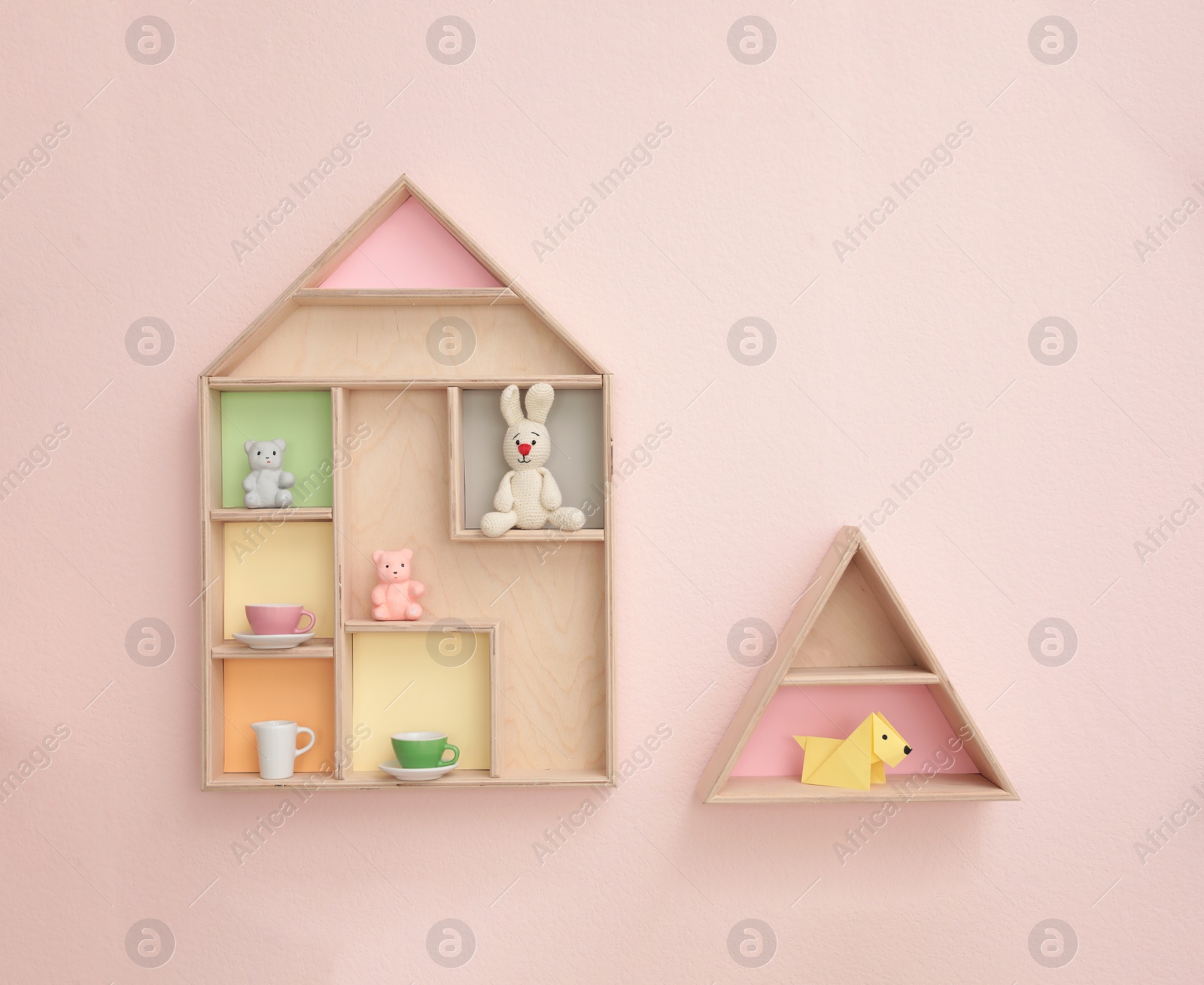 Photo of Stylish house shaped shelves with toys on pink wall. Baby room interior design