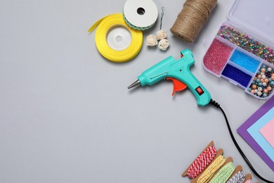 Photo of Hot glue gun and handicraft materials on grey background, flat lay. Space for text