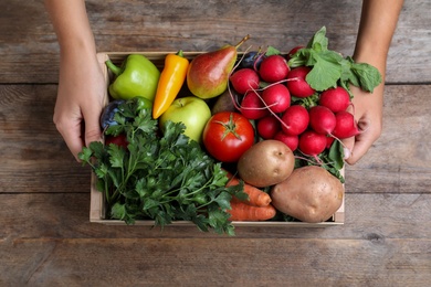 Photo of Farmer with crate full of different vegetables and fruits at wooden table, closeup. Harvesting time