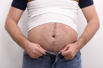 Man wearing tight t-shirt and jeans on white background, closeup. Overweight problem