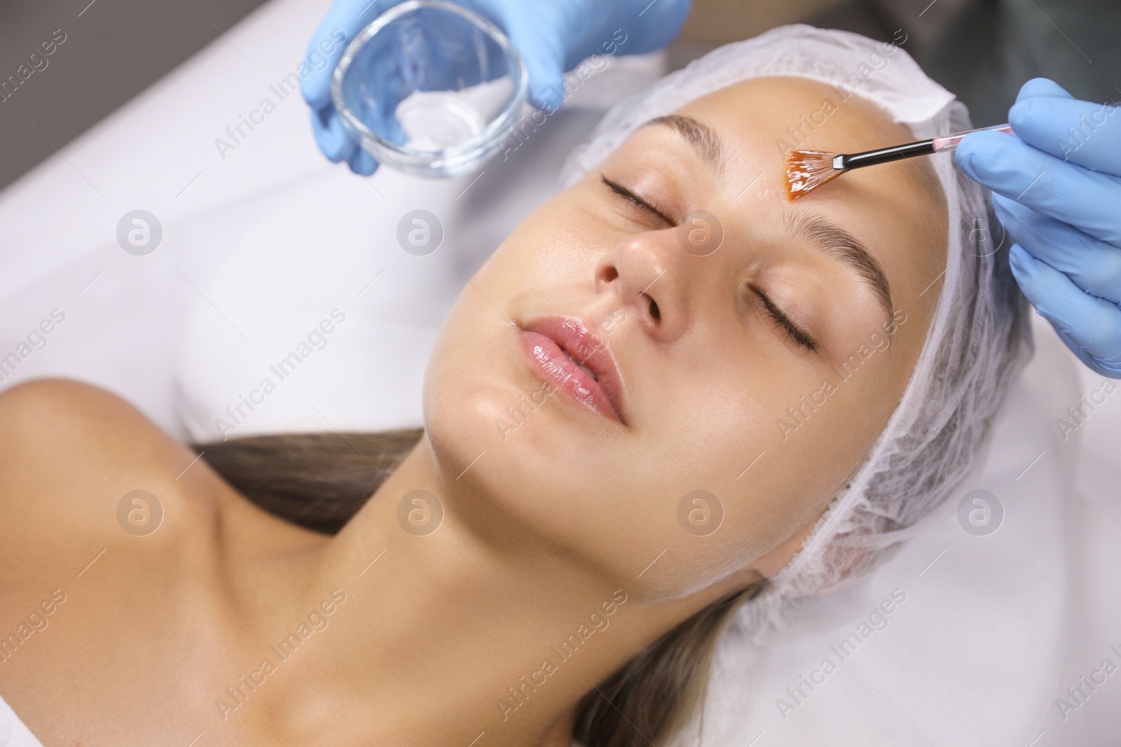 Photo of Cosmetologist applying chemical peel product on client's face in salon