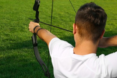Photo of Man with bow and arrow practicing archery on green grass, back view