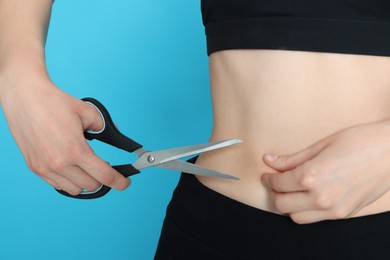 Slim woman with scissors on light blue background, closeup. Weight loss surgery