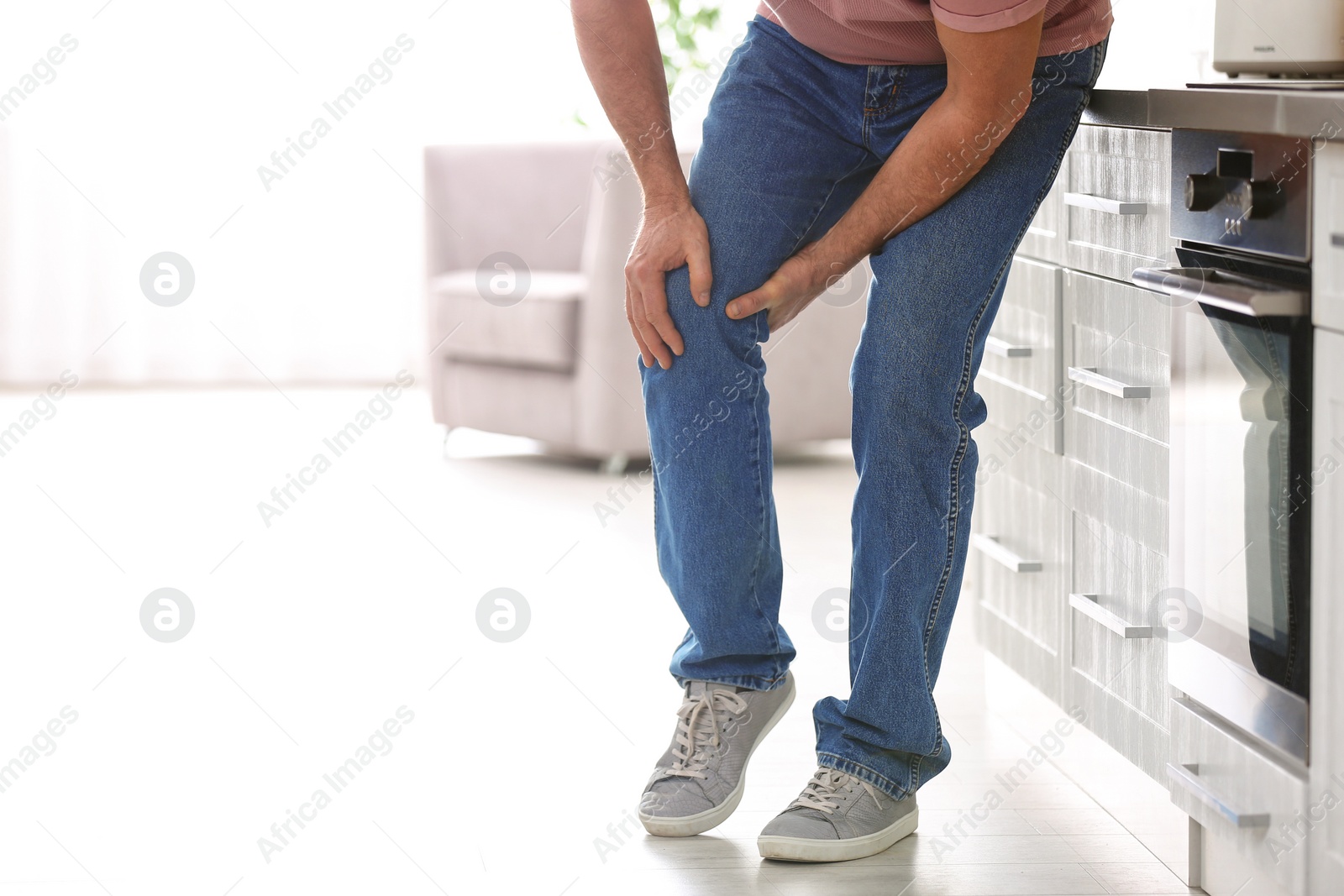 Photo of Senior man suffering from knee pain in kitchen, closeup. Space for text