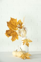 Composition with beautiful autumn leaves and pumpkins on table against white brick wall
