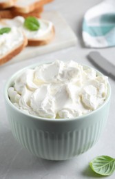 Bowl of tasty cream cheese on grey table