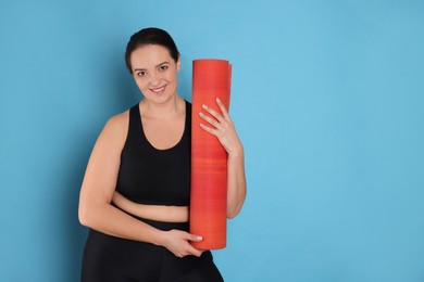 Photo of Happy overweight woman with yoga mat on light blue background. Space for text