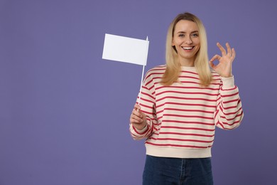 Photo of Happy woman with blank white flag showing OK gesture on violet background. Mockup for design