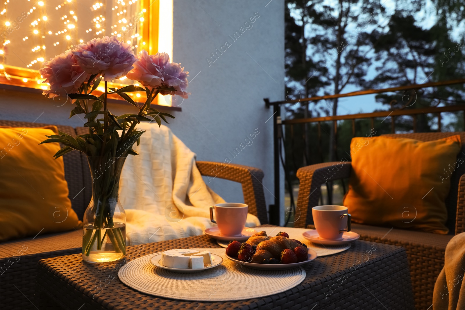 Photo of Rattan table with drink, food and flowers on outdoor terrace in evening