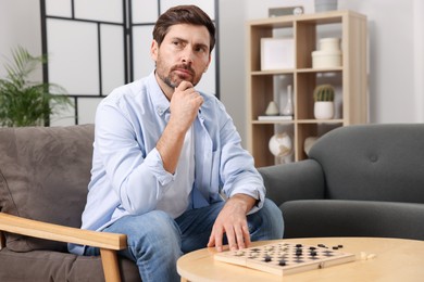 Photo of Thoughtful man playing checkers in armchair at home