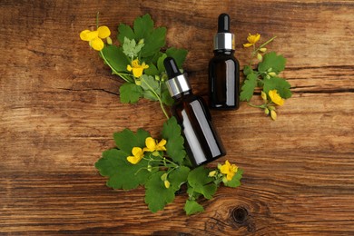 Photo of Bottles of natural celandine oil and flowers on wooden table, flat lay