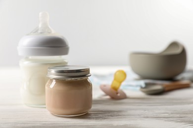 Photo of Jar with healthy baby food and bottle of milk on white wooden table. Space for text