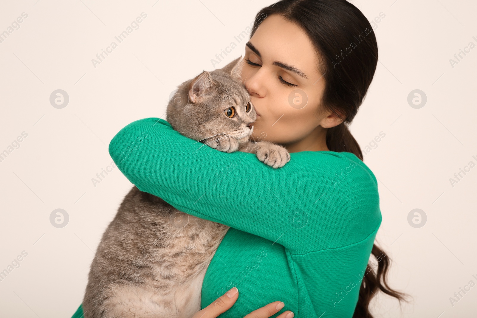 Photo of Young woman kissing her adorable cat on light background