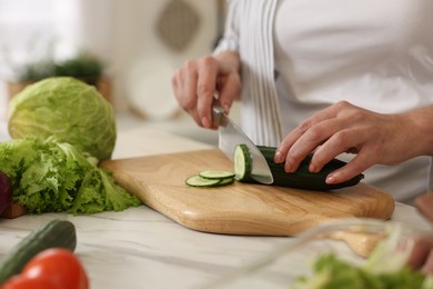 Photo of Woman cutting cucumber at white marble table, closeup