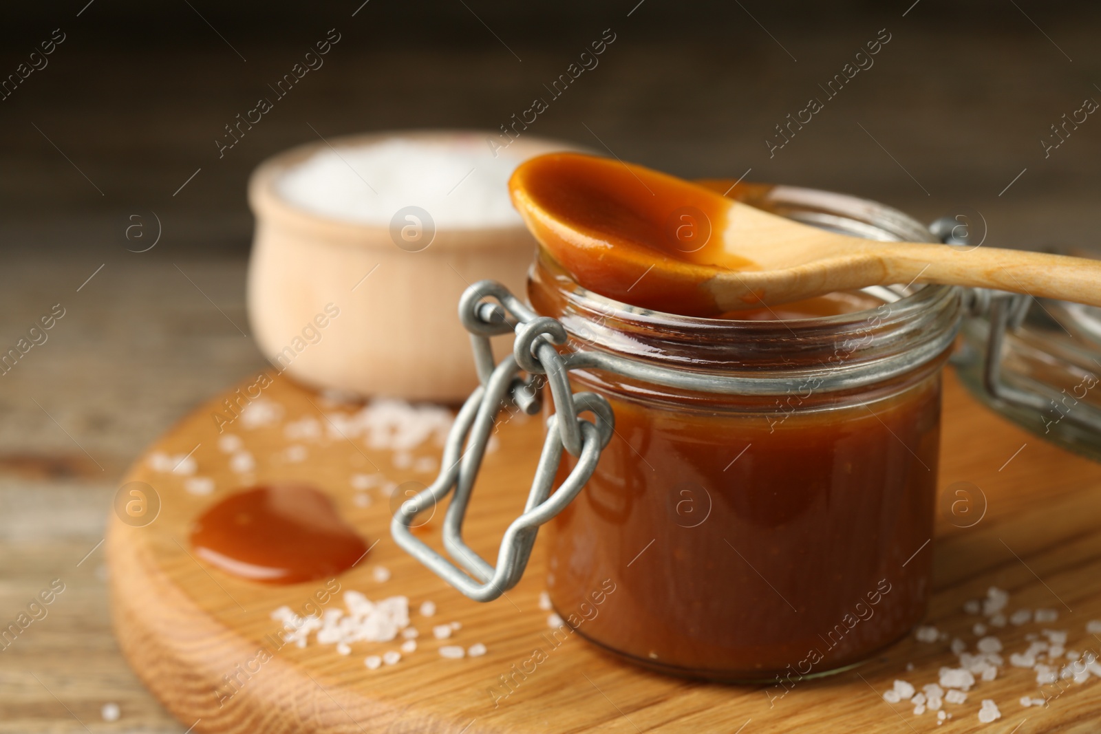 Photo of Jar and spoon with tasty salted caramel on table, closeup