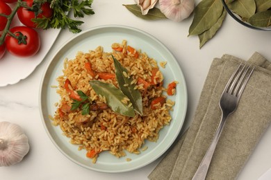 Photo of Delicious pilaf, bay leaves, ingredients and fork on white table, flat lay