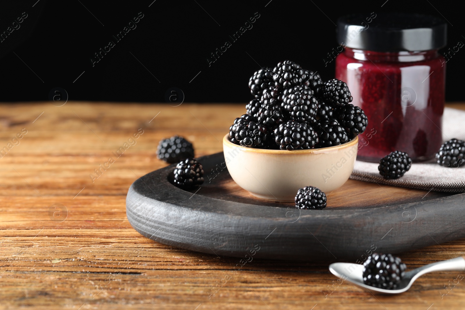 Photo of Fresh ripe blackberries and tasty jam on wooden table. Space for text