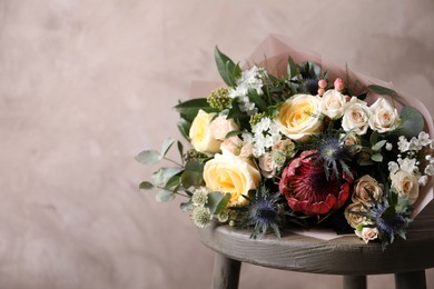 Photo of Beautiful bouquet with roses on chair near beige wall. Space for text