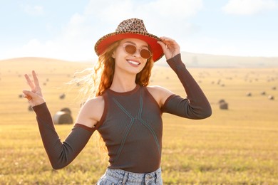 Photo of Beautiful happy hippie woman in hat showing peace sign in field