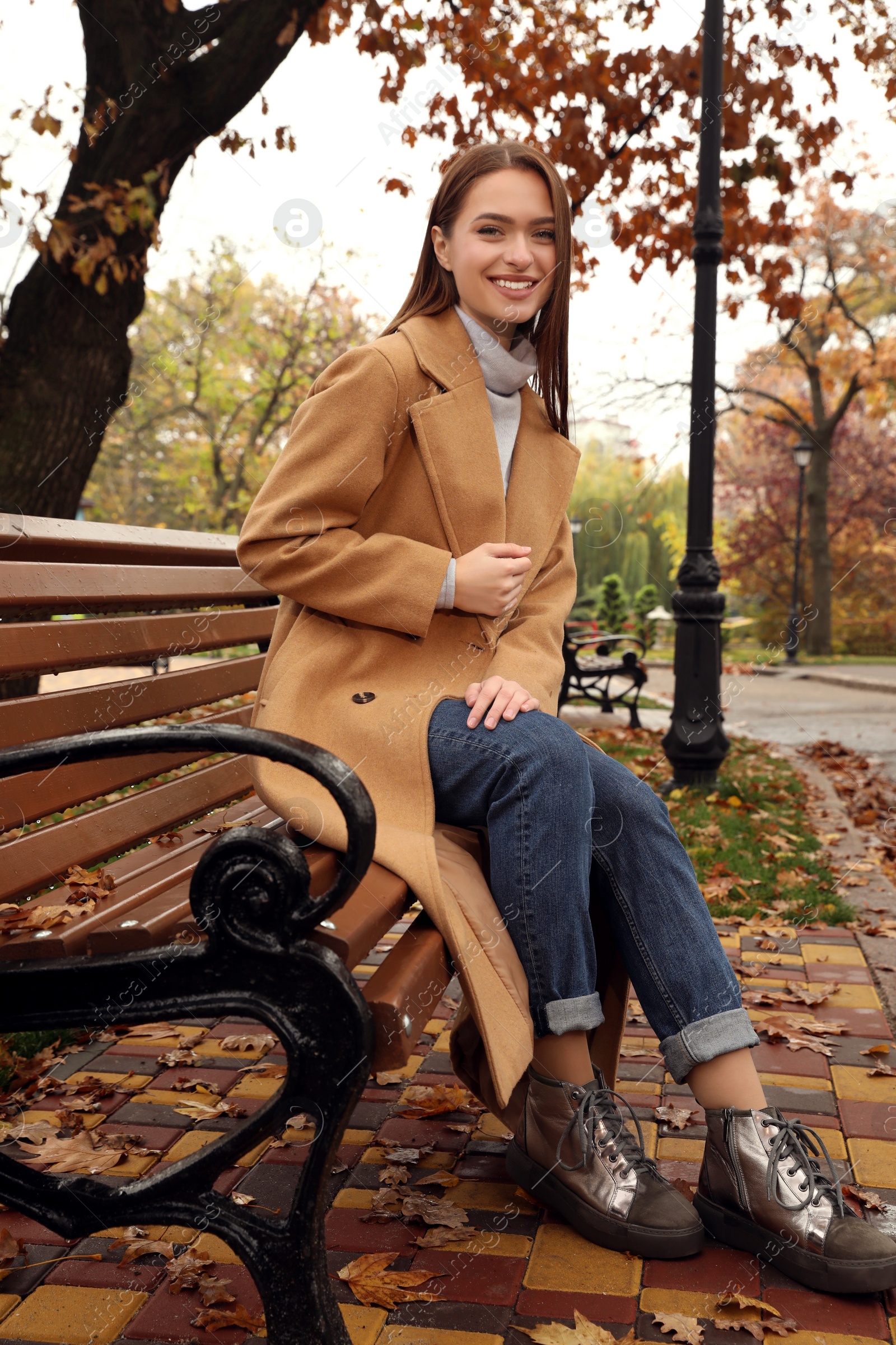 Photo of Beautiful young woman wearing stylish clothes on bench in autumn park