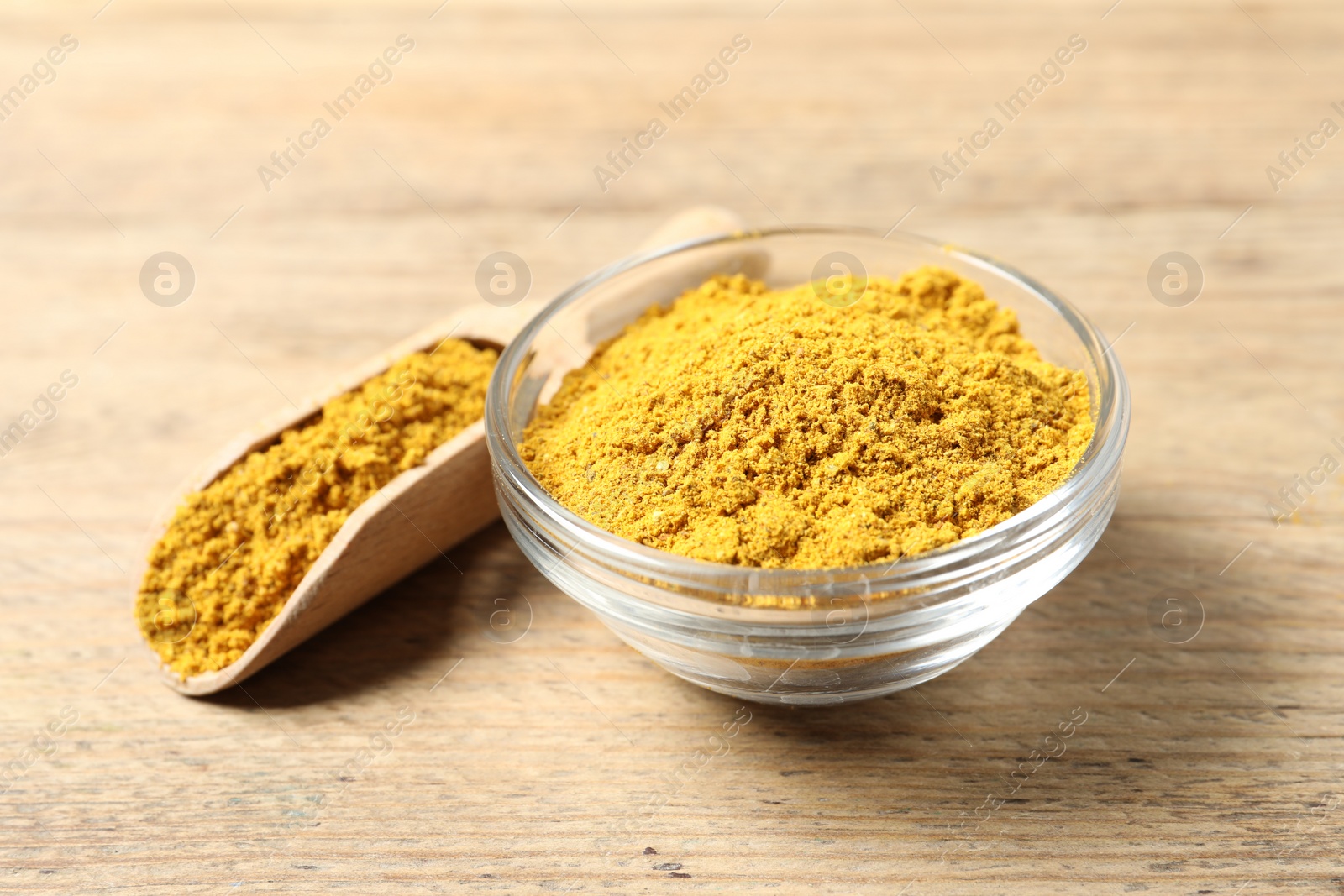 Photo of Curry powder in bowl and scoop on wooden table, closeup