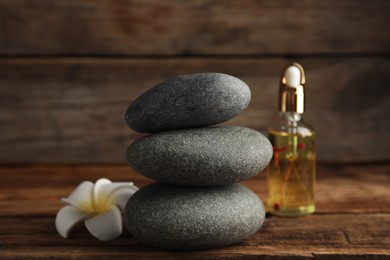 Stack of grey spa stones, flower and oil on wooden table