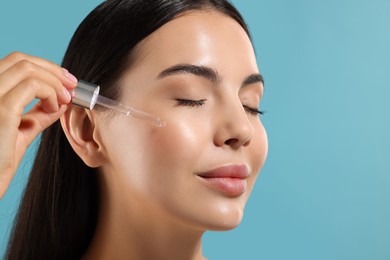 Photo of Beautiful young woman applying serum onto her face on light blue background, closeup. Space for text