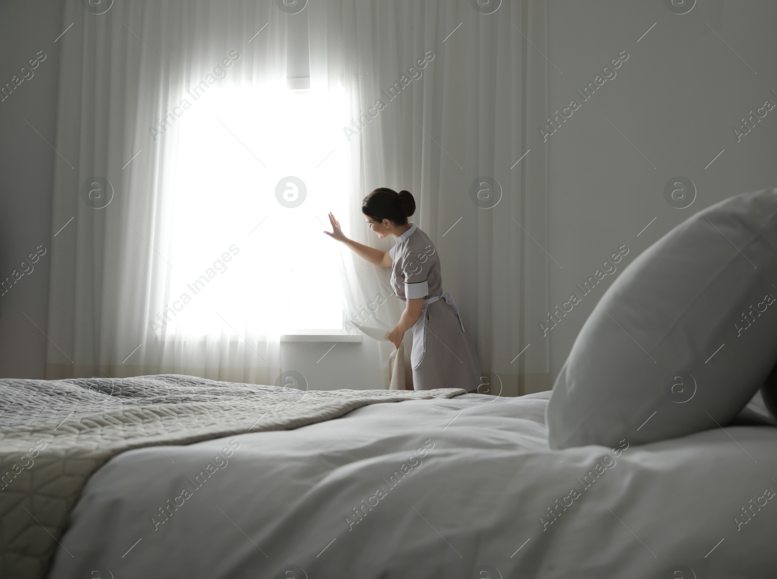 Photo of Young maid opening curtains in hotel room