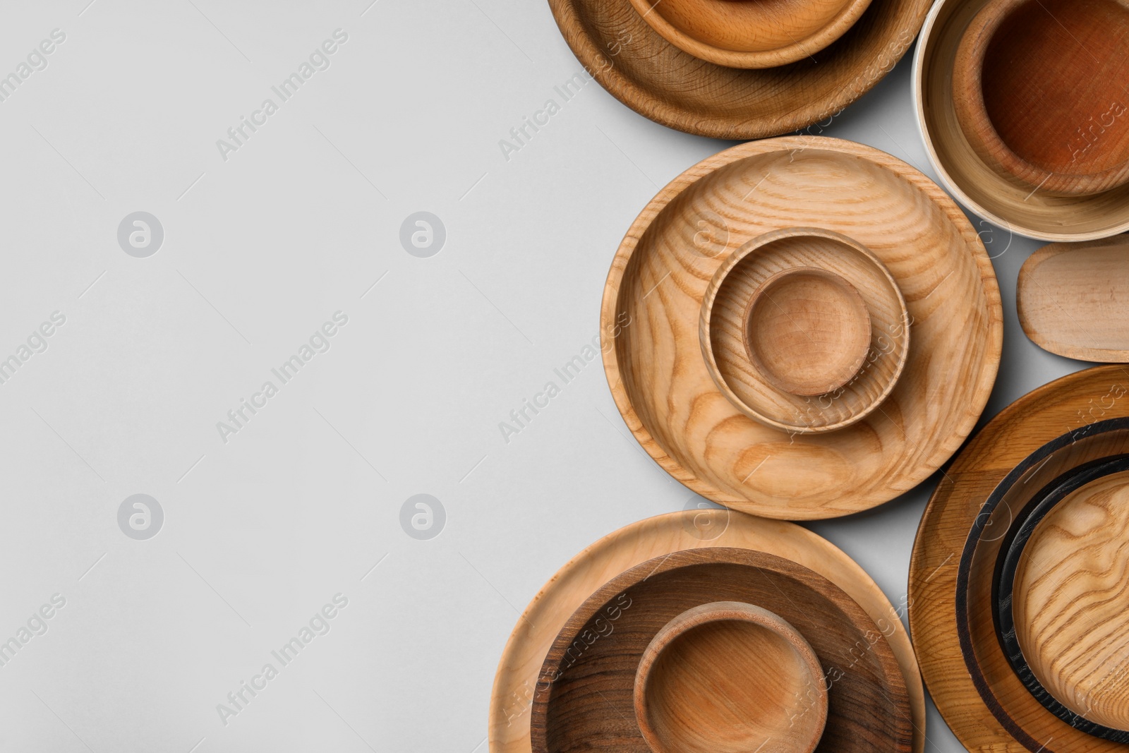 Photo of Set of different wooden dishes on light grey background, flat lay with space for text. Cooking utensils