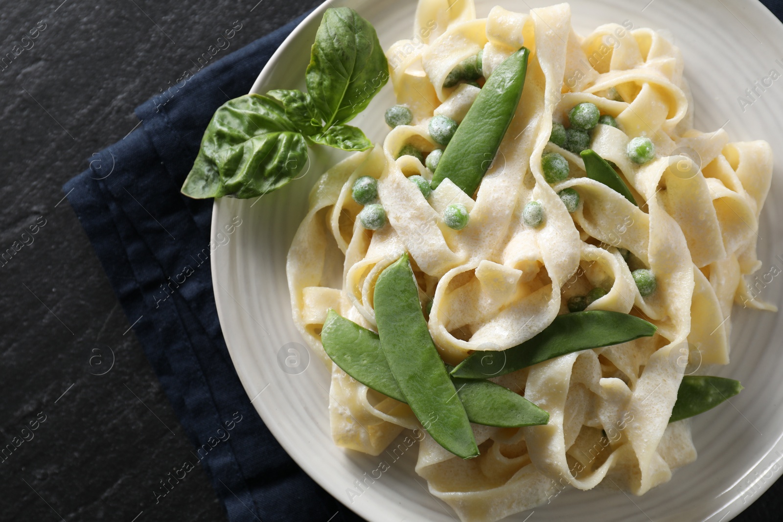 Photo of Delicious pasta with green peas and creamy sauce on black table, top view