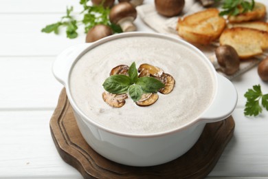 Photo of Fresh homemade mushroom soup in ceramic pot on white wooden table