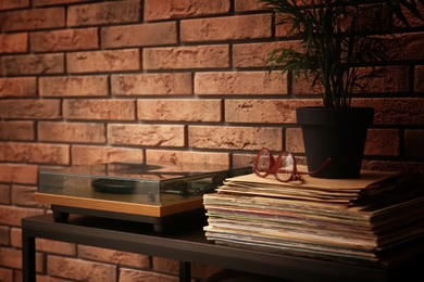 Photo of Stylish turntable and vinyl records on shelving unit near red brick wall