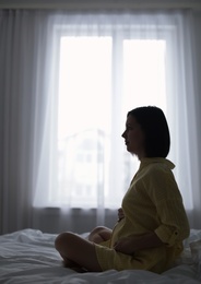 Beautiful pregnant woman sitting on bed at home