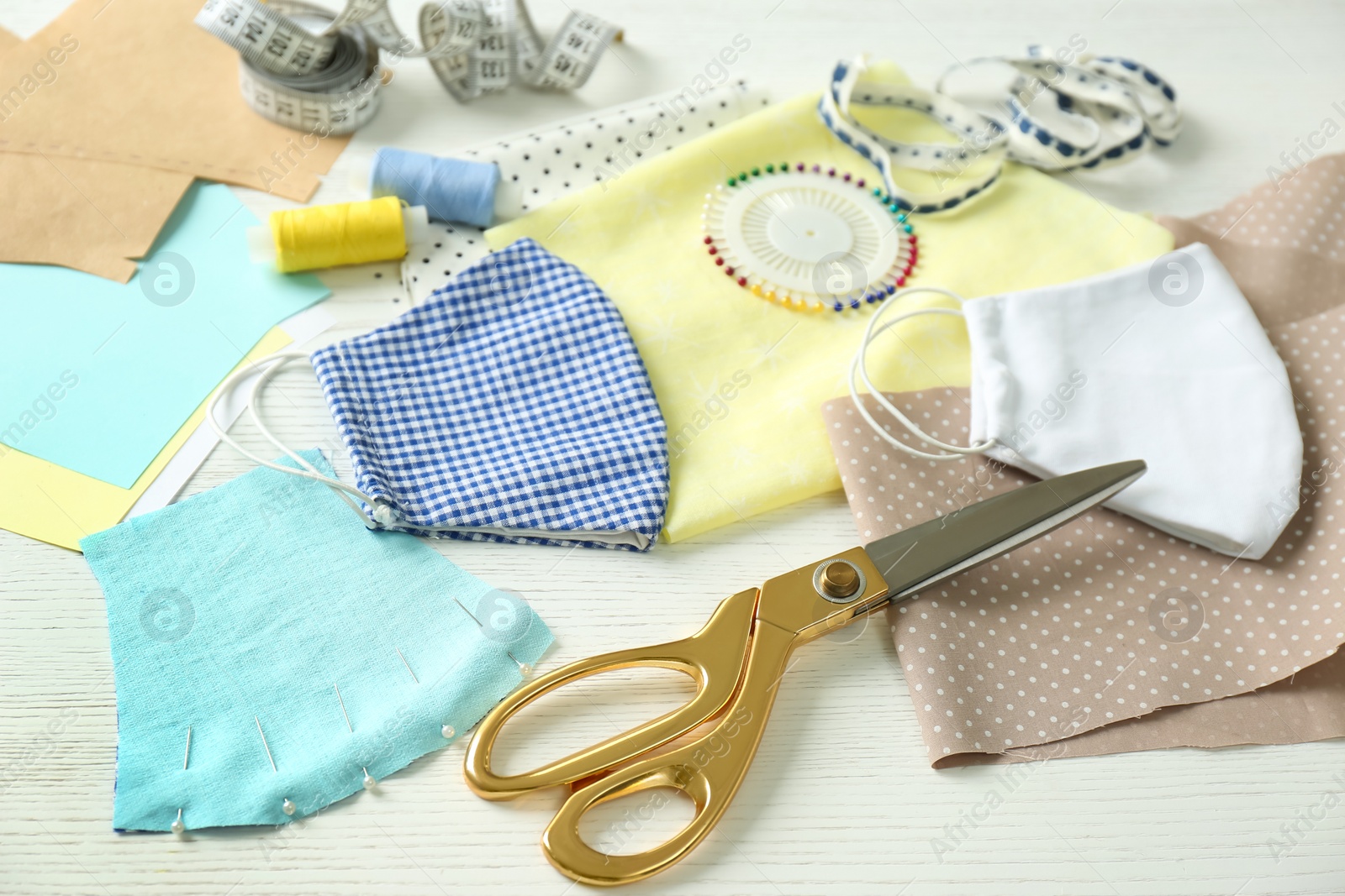 Photo of Fabric, sewing accessories and cloth masks on white wooden table. Personal protective equipment during COVID-19 pandemic