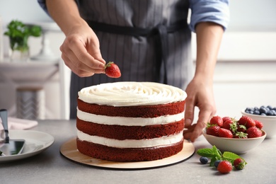 Woman decorating delicious homemade red velvet cake with strawberry at table