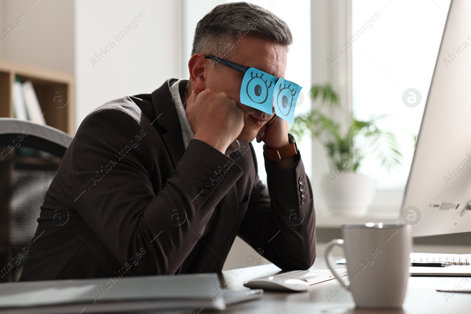 Photo of Man with fake eyes painted on sticky notes snoozing at workplace in office