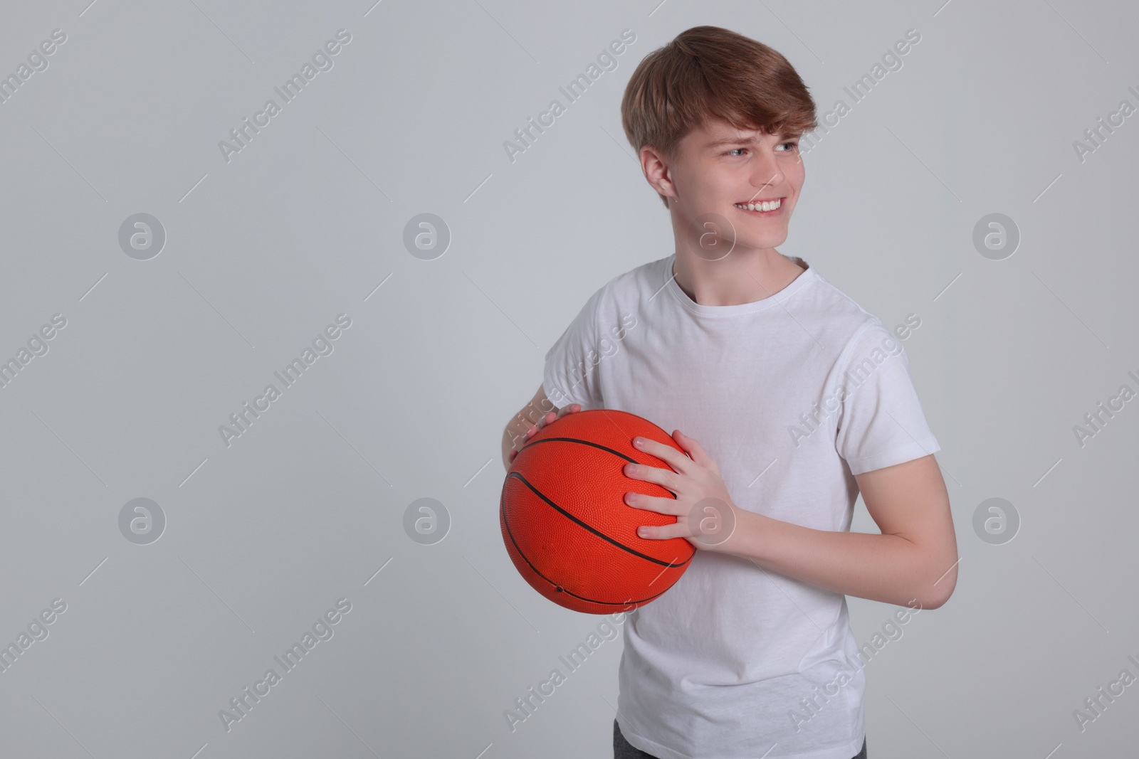 Photo of Teenage boy with basketball ball on light grey background. Space for text