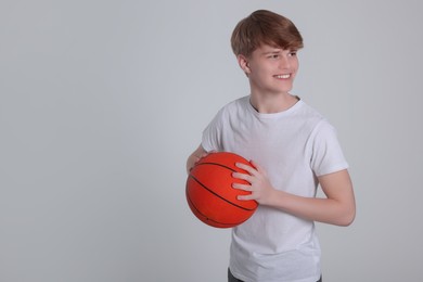 Photo of Teenage boy with basketball ball on light grey background. Space for text