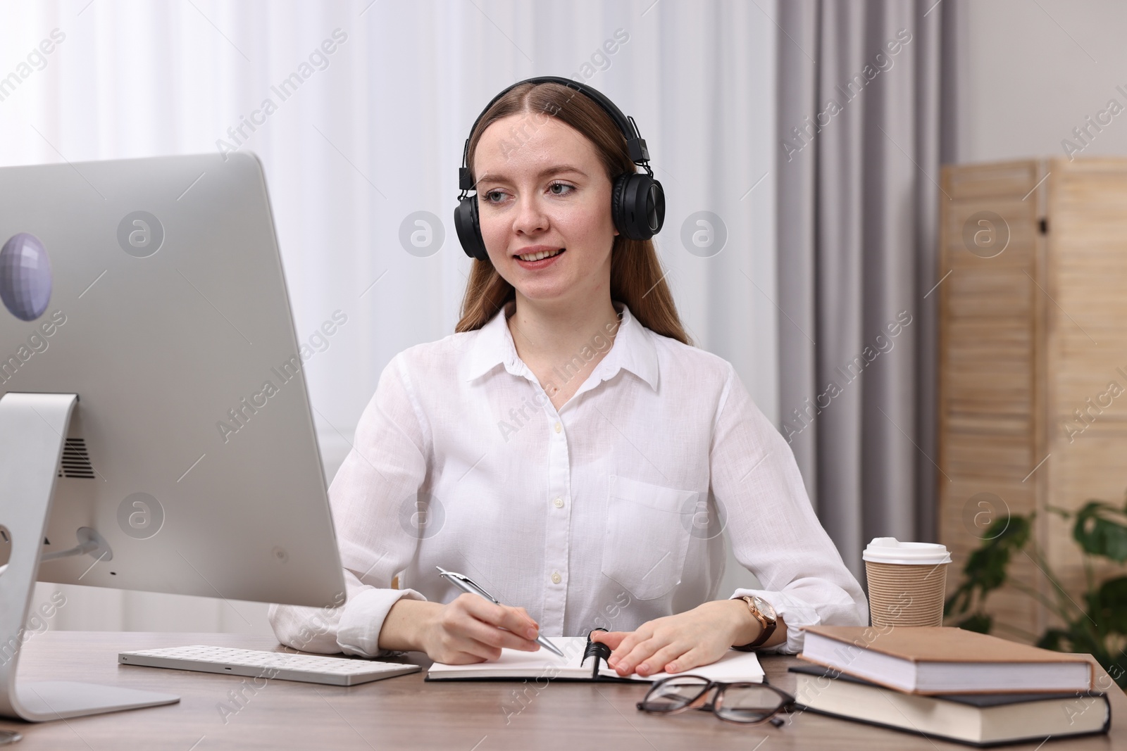 Photo of E-learning. Young woman taking notes during online lesson at wooden table indoors